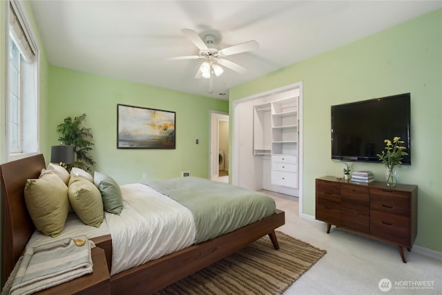 bedroom with light colored carpet, ceiling fan, a walk in closet, and baseboards