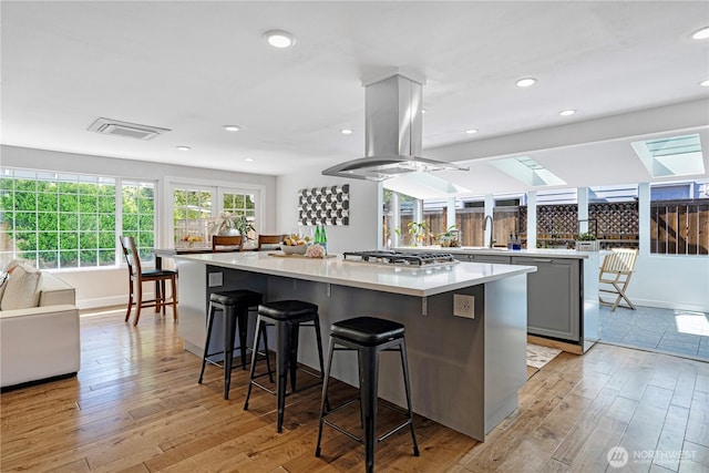 kitchen with a spacious island, light wood-type flooring, island range hood, stainless steel gas cooktop, and recessed lighting