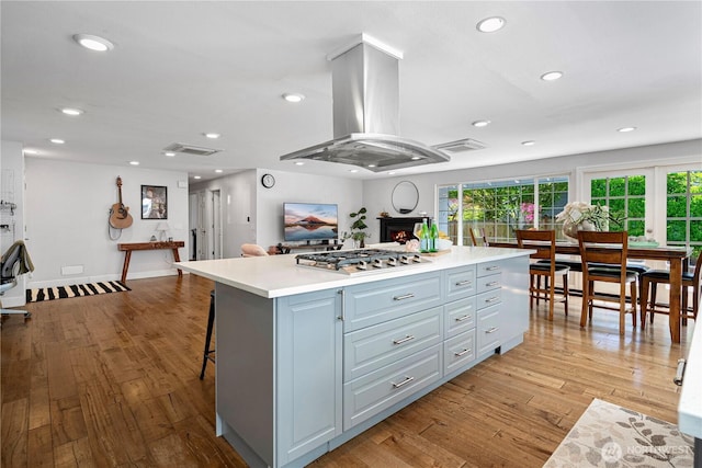 kitchen with island exhaust hood, stainless steel gas cooktop, light wood-style floors, light countertops, and recessed lighting