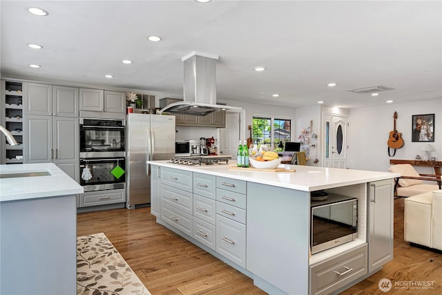 kitchen featuring stainless steel appliances, island exhaust hood, a sink, recessed lighting, and gray cabinetry