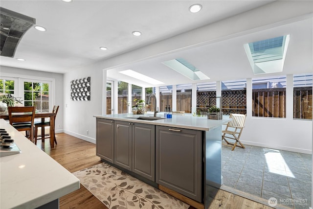 kitchen featuring a skylight, a sink, gray cabinetry, light countertops, and baseboards