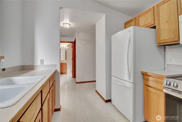 kitchen with a sink, stainless steel electric stove, freestanding refrigerator, light countertops, and baseboards