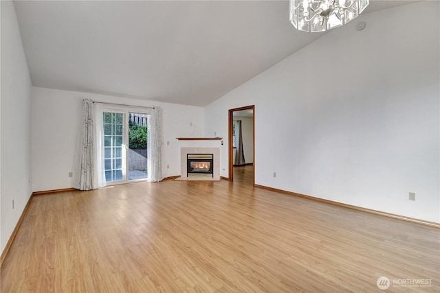unfurnished living room featuring light wood-style flooring, a chandelier, a tiled fireplace, baseboards, and high vaulted ceiling