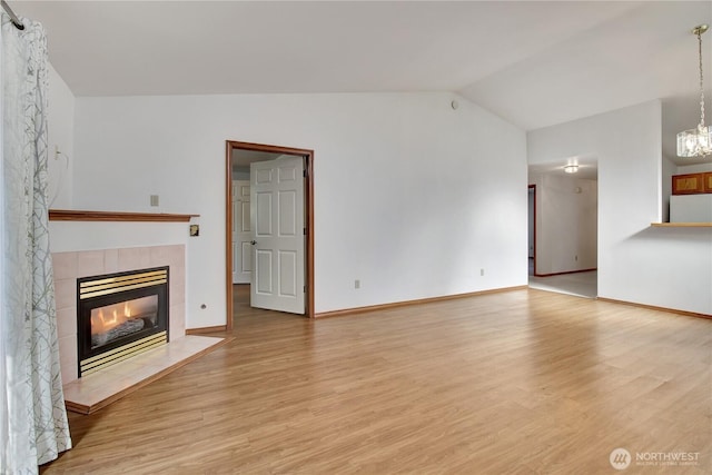 unfurnished living room featuring lofted ceiling, a tiled fireplace, light wood finished floors, baseboards, and a chandelier