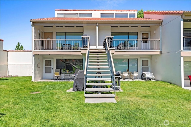 rear view of house with stairs, a lawn, and stucco siding