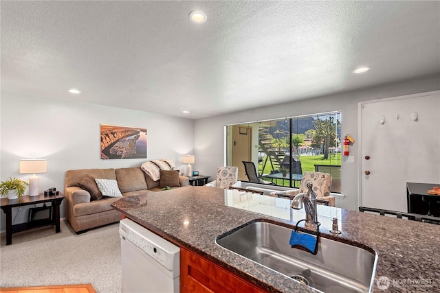 kitchen with white dishwasher, a sink, open floor plan, a textured ceiling, and dark stone counters