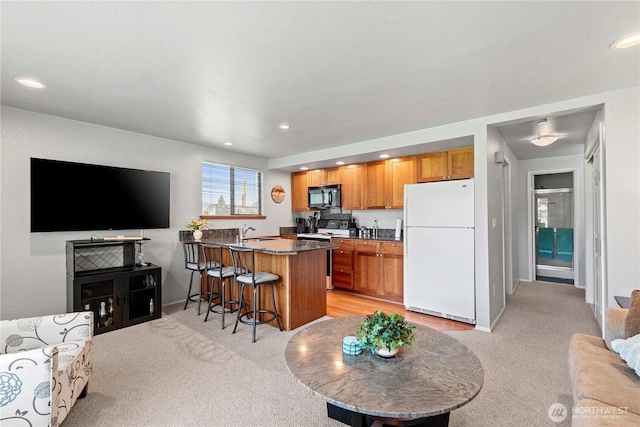 kitchen with white appliances, light colored carpet, a peninsula, a breakfast bar, and brown cabinets