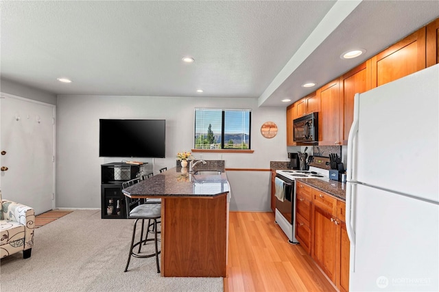 kitchen featuring white appliances, recessed lighting, a sink, dark stone counters, and a kitchen island with sink