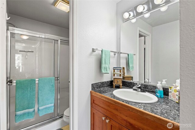 full bathroom with a stall shower, toilet, vanity, and a textured wall