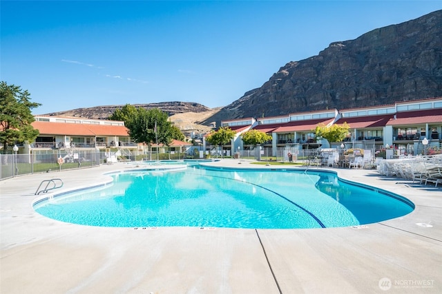 community pool featuring a mountain view, fence, and a patio area
