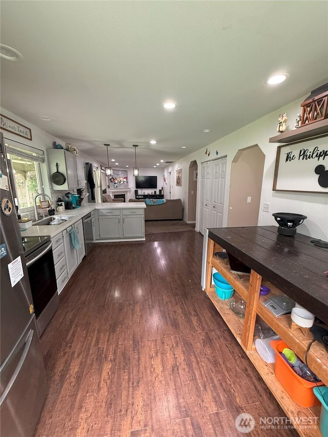 21614 82nd Avenue Ct E, Spanaway, WA 68718 - kitchen featuring arched walkways, appliances with stainless steel finishes, a peninsula, a sink, and dark wood-style floors