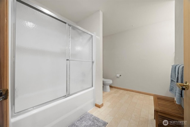 bathroom featuring toilet, bath / shower combo with glass door, and baseboards