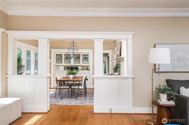 dining space with decorative columns, ornamental molding, light wood-style flooring, and a chandelier