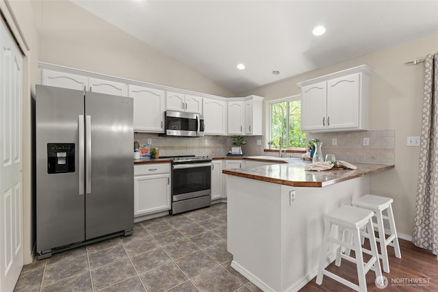 kitchen with appliances with stainless steel finishes, a peninsula, white cabinetry, vaulted ceiling, and a sink