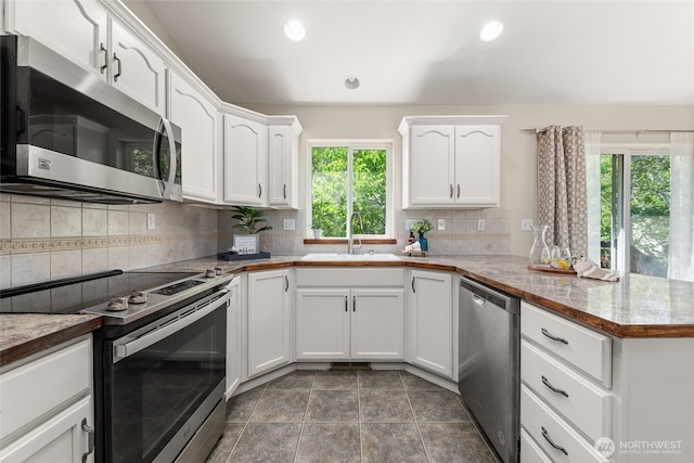 kitchen with appliances with stainless steel finishes, a sink, a peninsula, white cabinets, and backsplash