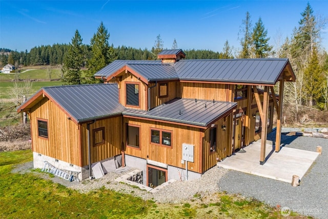 back of house with metal roof, a standing seam roof, and a patio
