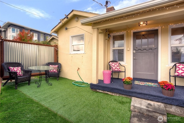 doorway to property featuring stucco siding, fence, and a chimney