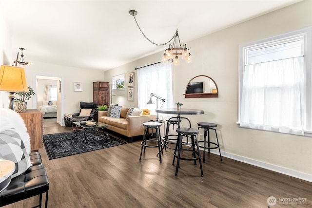 living area with dark wood-style flooring, a chandelier, and baseboards