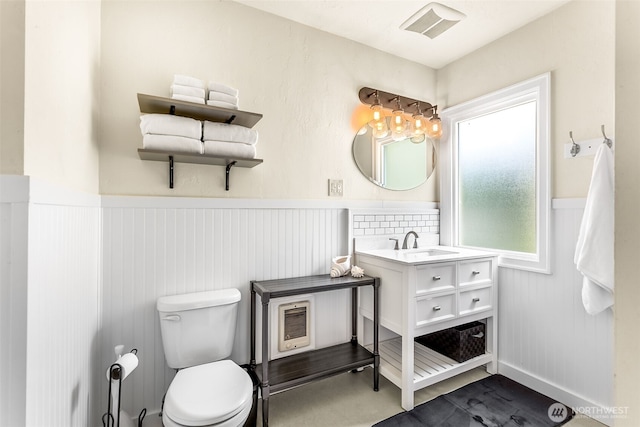 bathroom featuring wainscoting, toilet, vanity, and heating unit