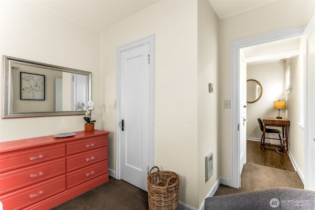 hallway featuring dark carpet and baseboards
