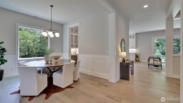 dining room with a wainscoted wall, light wood-style flooring, healthy amount of natural light, a decorative wall, and a chandelier