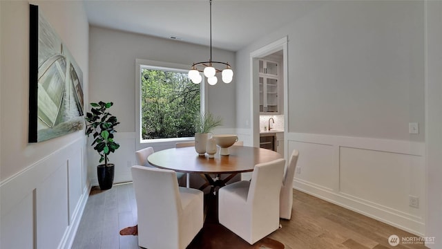 dining room with a decorative wall, a wainscoted wall, wood finished floors, and a chandelier