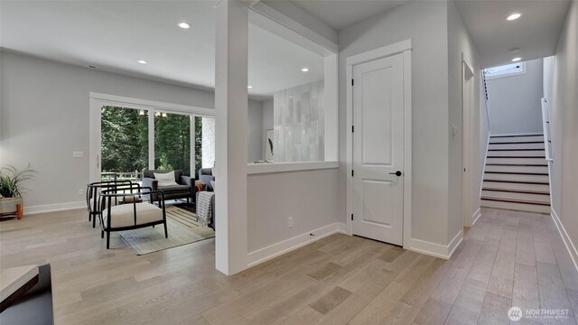 hallway featuring light wood-style flooring, baseboards, recessed lighting, and stairway