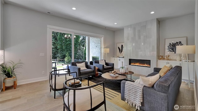 living room featuring light wood-style floors, a tiled fireplace, recessed lighting, and baseboards