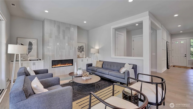 living room with light wood-style floors, recessed lighting, a tile fireplace, and baseboards
