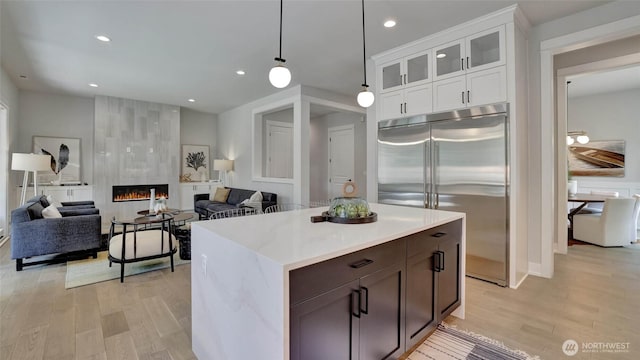 kitchen featuring stainless steel built in fridge, light wood-style floors, light countertops, white cabinets, and a tile fireplace