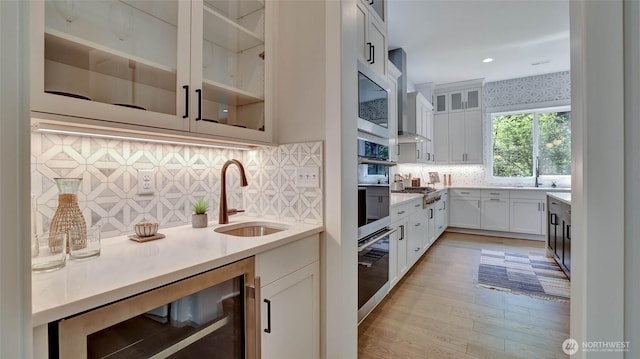 kitchen with a sink, beverage cooler, decorative backsplash, light countertops, and white cabinets