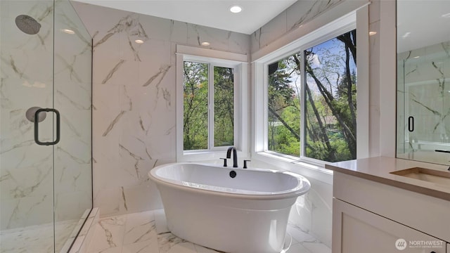 full bathroom featuring a marble finish shower, a freestanding bath, healthy amount of natural light, vanity, and tile walls