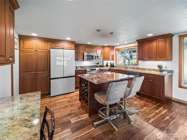 kitchen featuring stainless steel appliances, wood finished floors, light stone countertops, brown cabinetry, and recessed lighting