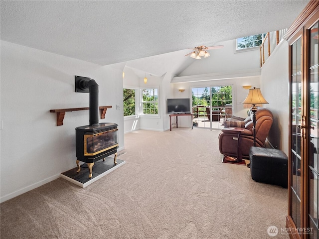 carpeted living room with a wood stove, vaulted ceiling, a textured ceiling, a ceiling fan, and baseboards