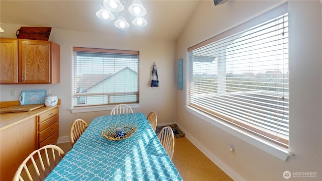 carpeted dining space with baseboards, a chandelier, and vaulted ceiling