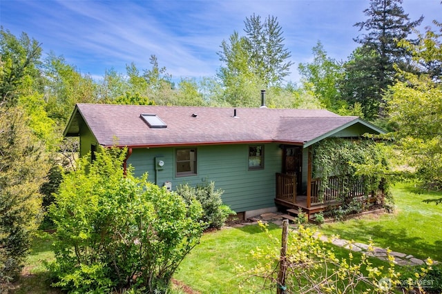 rear view of house with a deck, roof with shingles, and a yard
