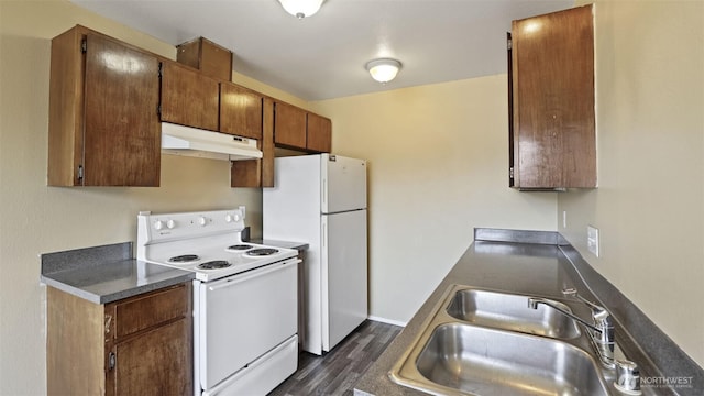 kitchen featuring under cabinet range hood, white appliances, a sink, dark wood-style flooring, and dark countertops
