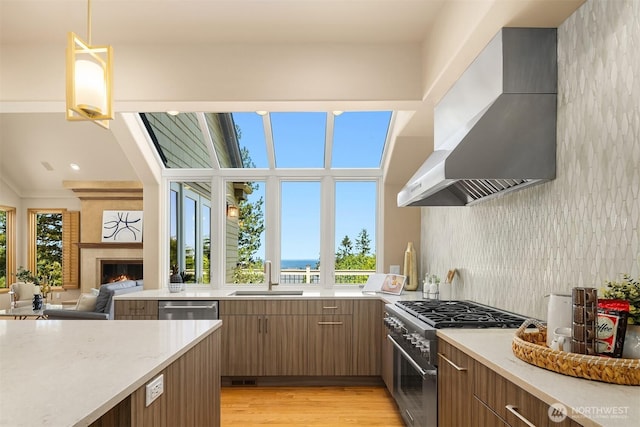 5874 169th Ave SE, Bellevue, WA 98006 - kitchen featuring wall chimney exhaust hood, stainless steel appliances, a sink, a warm lit fireplace, and brown cabinets