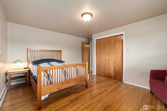 bedroom with wood finished floors, baseboards, a baseboard heating unit, and a closet