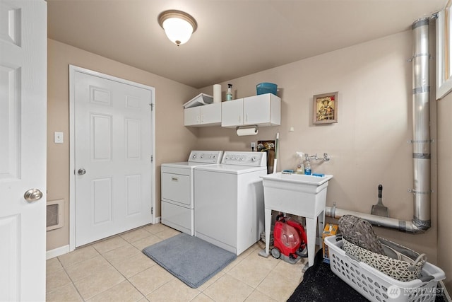 clothes washing area with washing machine and dryer, cabinet space, light tile patterned floors, and baseboards