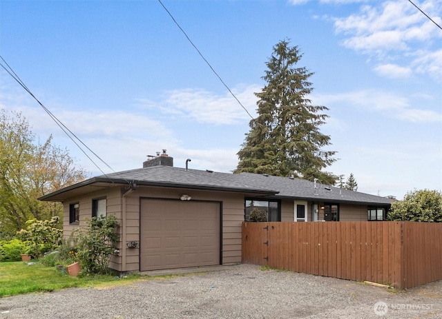 view of front of property with fence, a garage, a chimney, and gravel driveway