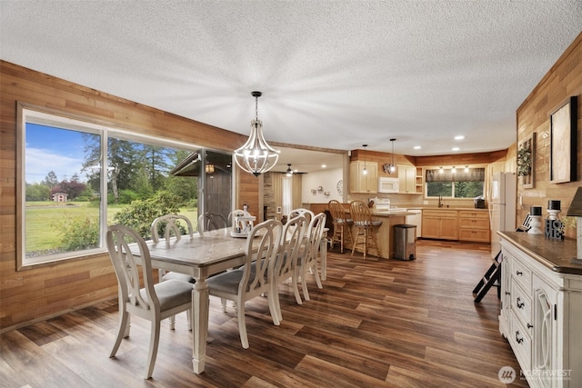 dining space featuring wood walls, a textured ceiling, a chandelier, dark wood-type flooring, and recessed lighting
