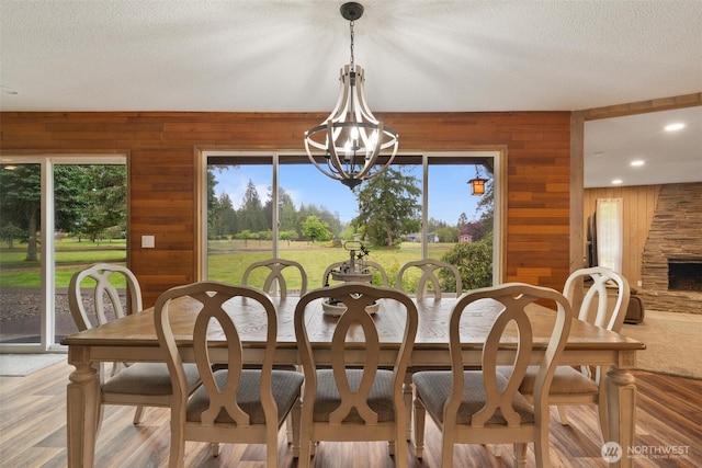 dining room with wooden walls, a chandelier, plenty of natural light, a textured ceiling, and recessed lighting