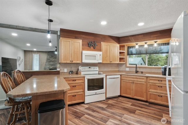 kitchen featuring white appliances, a sink, a peninsula, light brown cabinets, and dark wood-type flooring