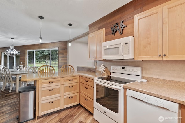 kitchen with white appliances, light brown cabinetry, a peninsula, light countertops, and wood walls