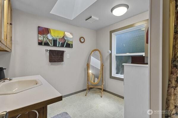 full bath featuring tile patterned floors, a skylight, baseboards, and vanity