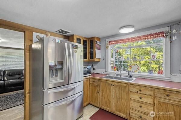 kitchen featuring appliances with stainless steel finishes, a sink, glass insert cabinets, light countertops, and brown cabinets