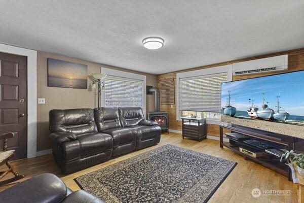 living room with a wood stove, a wall unit AC, wood finished floors, and baseboards