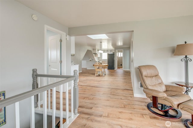 sitting room featuring light wood-style flooring, a skylight, baseboards, and an upstairs landing