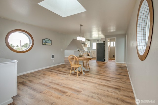 dining space featuring baseboards, light wood-style flooring, and a skylight